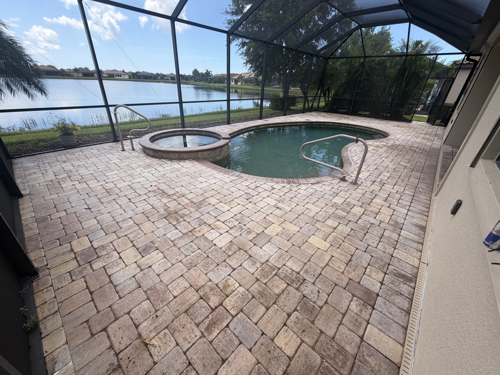 Blotchy paver pool deck and spa overlooking a lake in Venice, FL, before the failed sealer was stripped