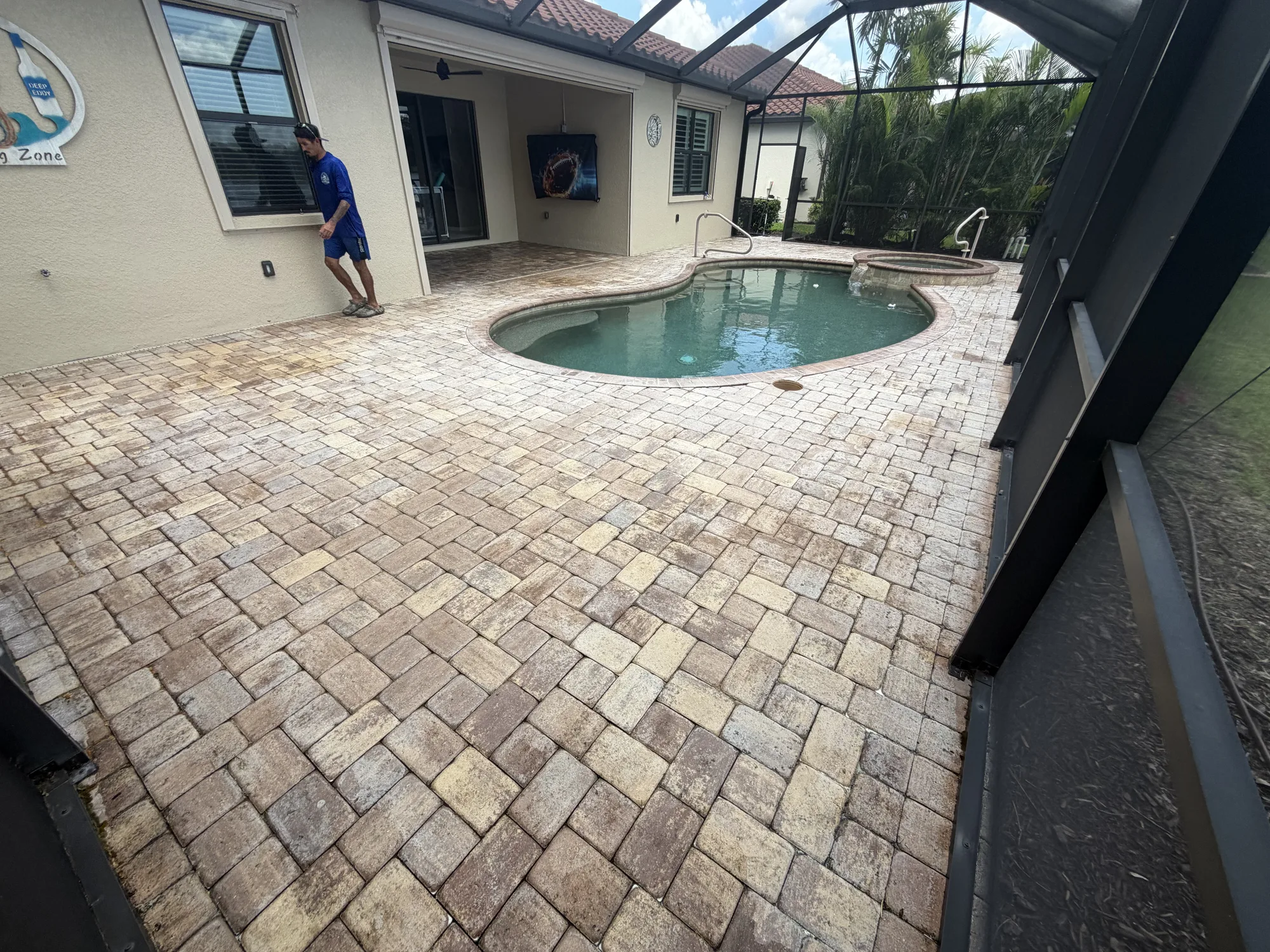Paver pool deck with patchy failed sealer beside the house in Venice, FL, a crew member walking the deck before stripping