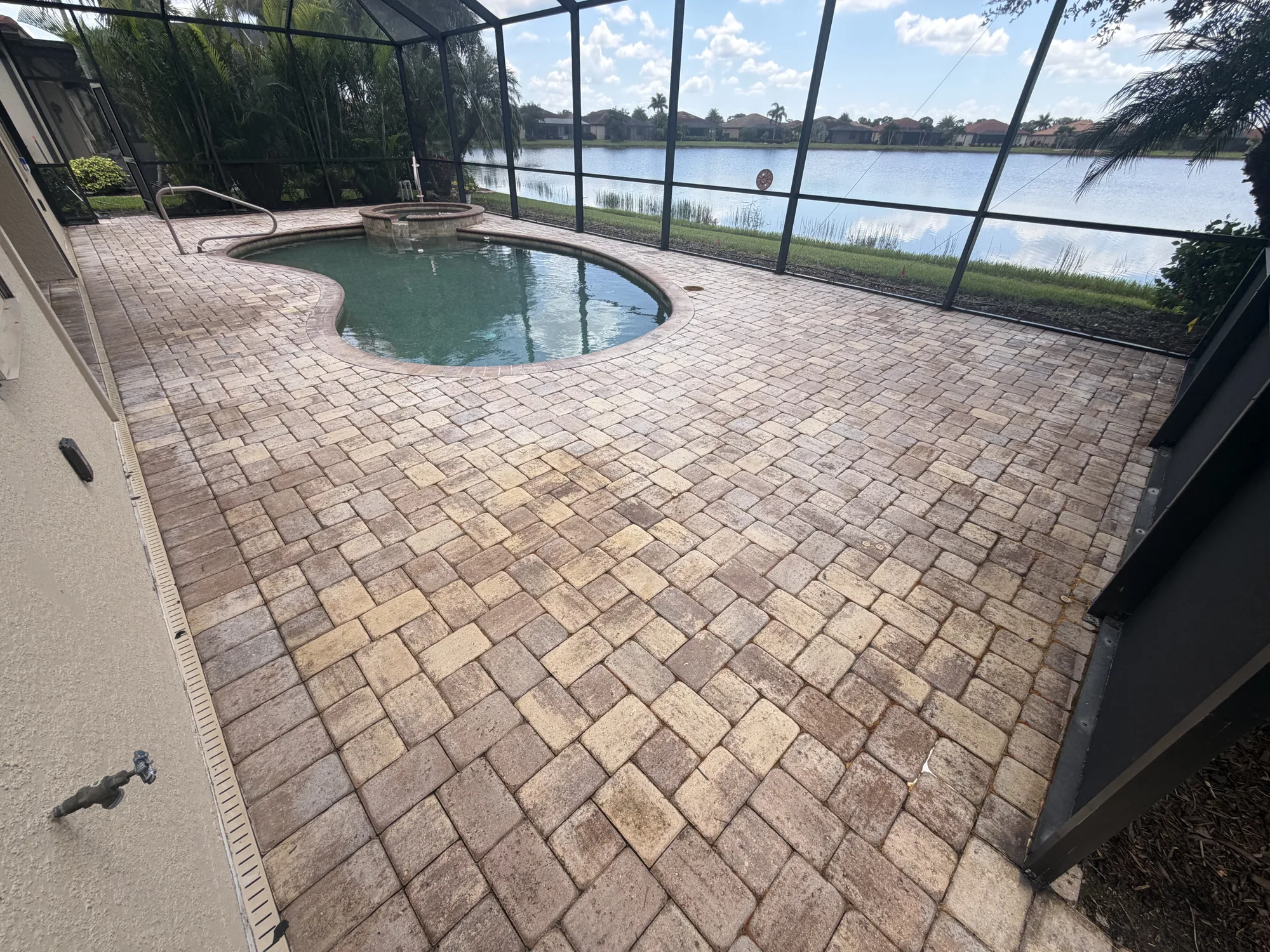Wide view of a paver pool deck overlooking a lake in Venice, FL, patchy failed sealer before stripping