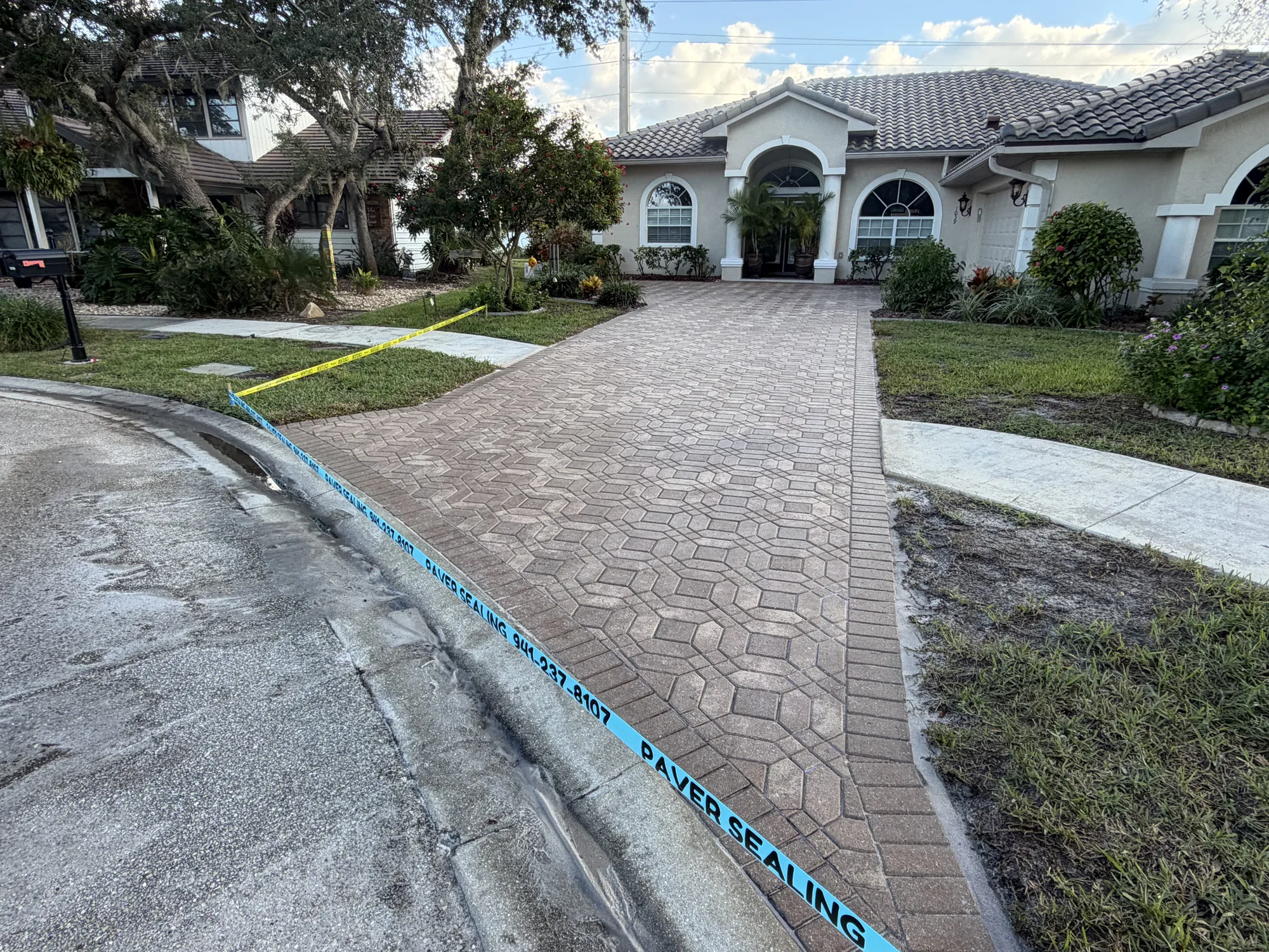 Same paver driveway in Venice, FL after stripping, resetting and sealing, curb taped off while the sealer cures