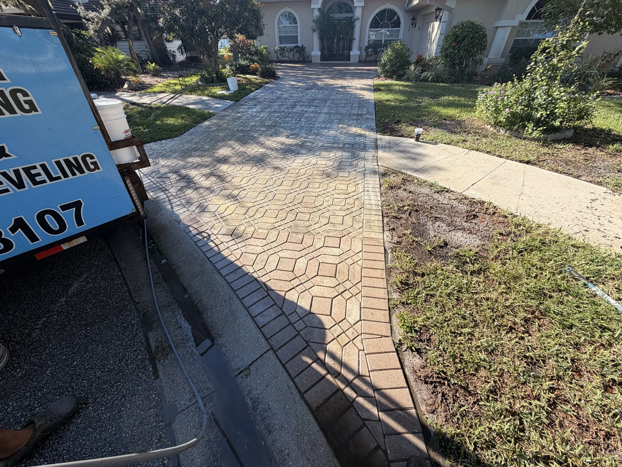 Faded paver driveway with failed sealer seen from the street in Venice, FL, the HD Paver Sealing trailer parked at the curb