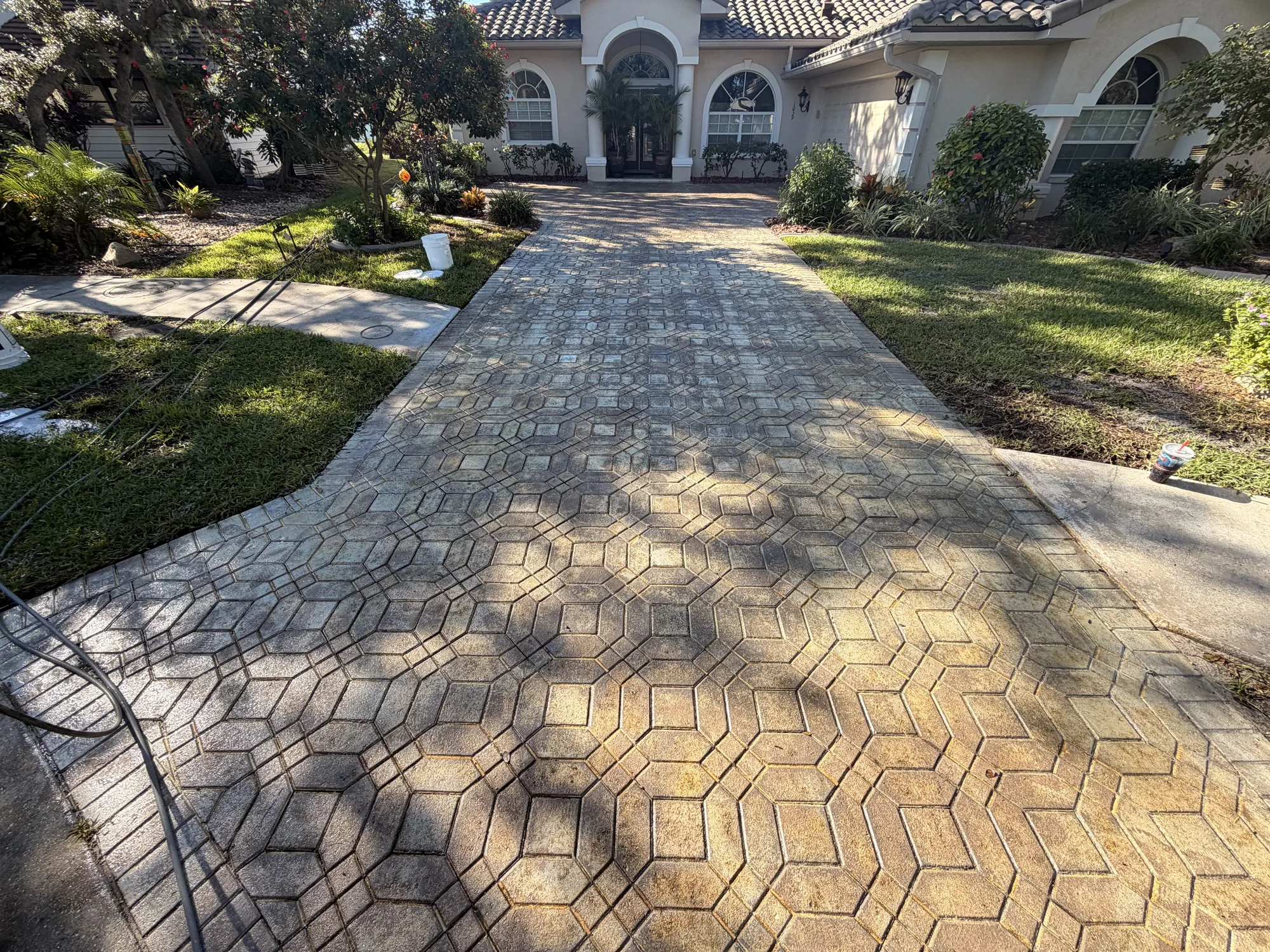 Paver driveway in Venice, FL with blotchy failed sealer and hoses laid out before stripping