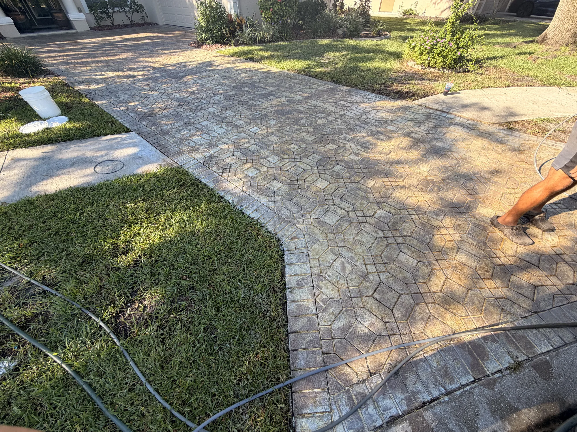 Worn paver driveway and walkway in Venice, FL with a crew member working the hose before stripping